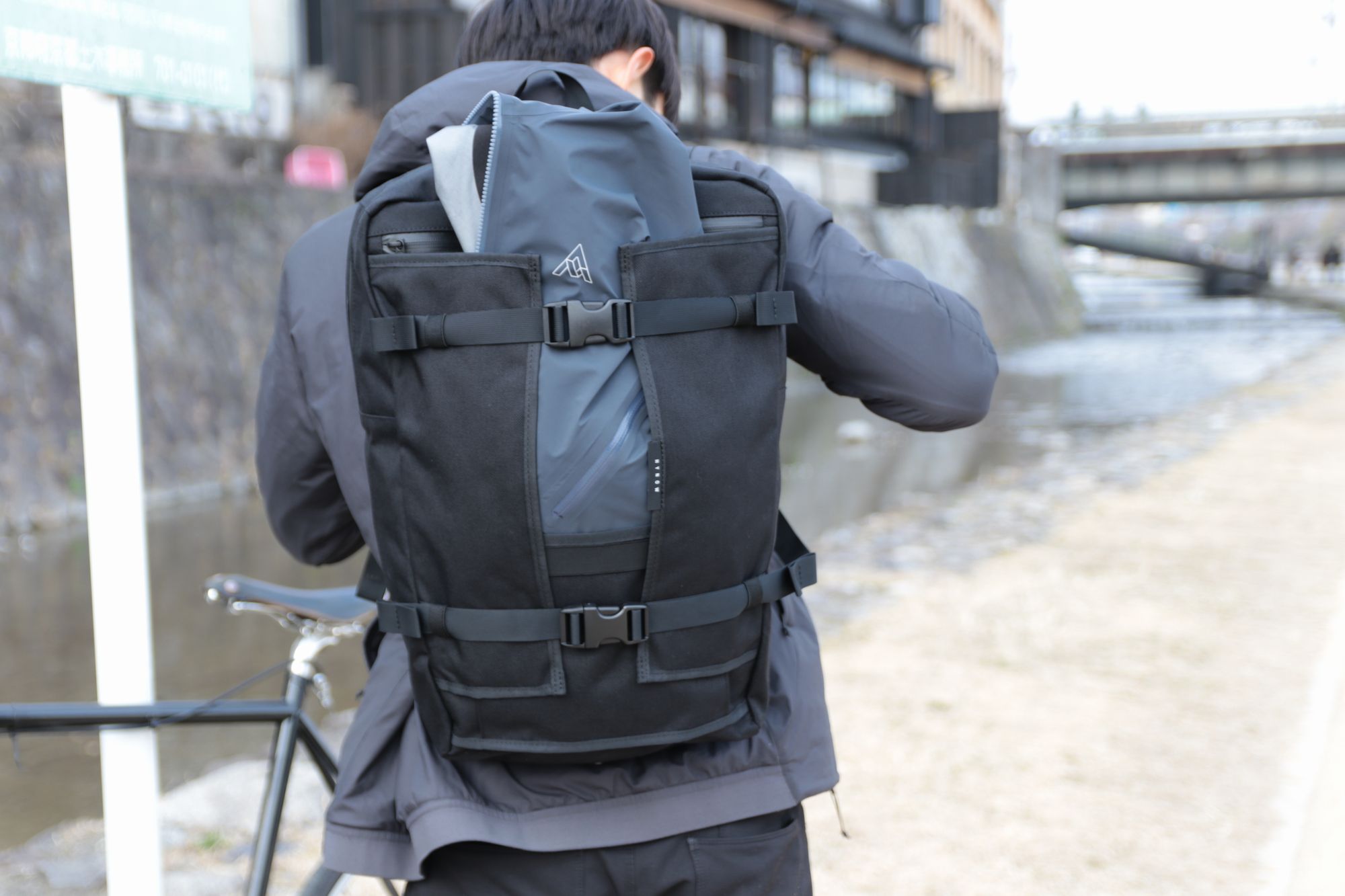HYNOW（ハイノウ）のバックパックRIVER（リバー）の観音開きのフラップにアウターを挟んだ後ろ姿